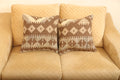 Brown and beige geometric wool square cushions set of two featuring traditional patterned designs on a beige sofa.