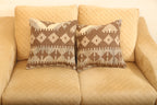 Brown and beige geometric wool square cushions set of two featuring traditional patterned designs on a beige sofa.