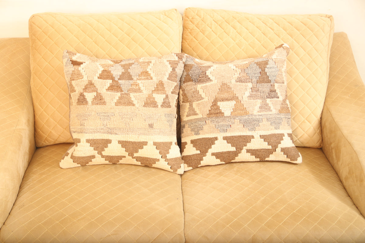 Beige and brown geometric wool square cushions set of two with a traditional patterned design on a beige sofa.