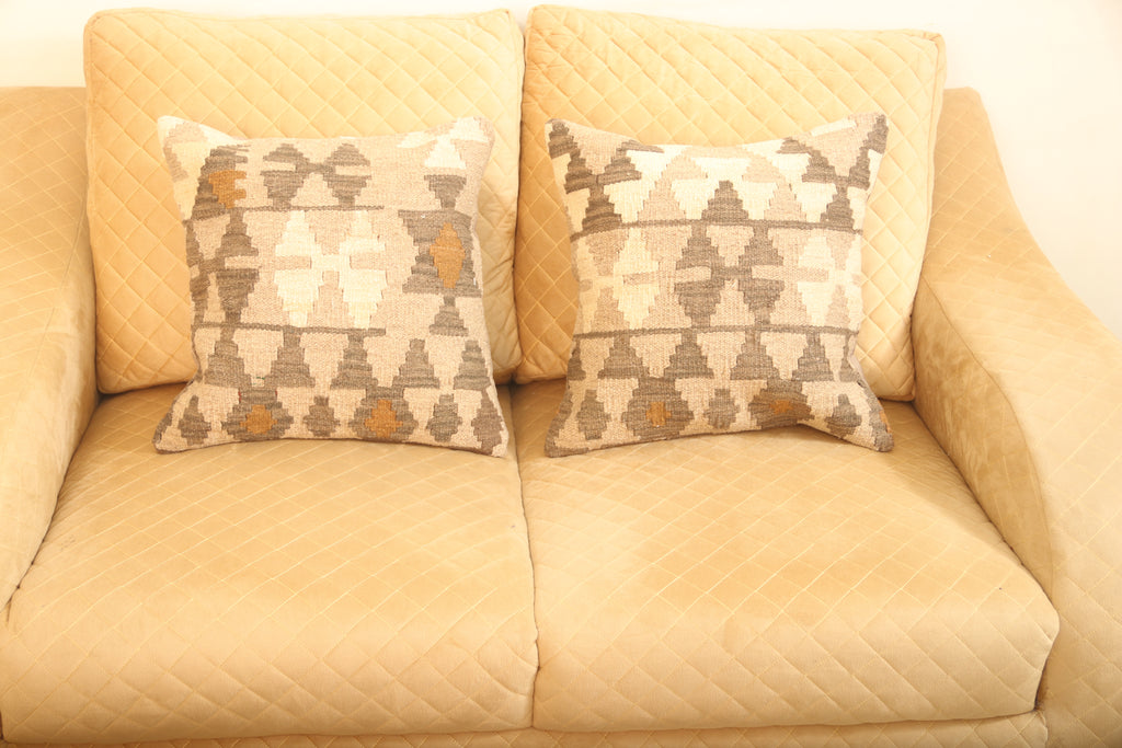 Beige and brown geometric wool square cushions set of two with a traditional patterned design on a beige sofa.