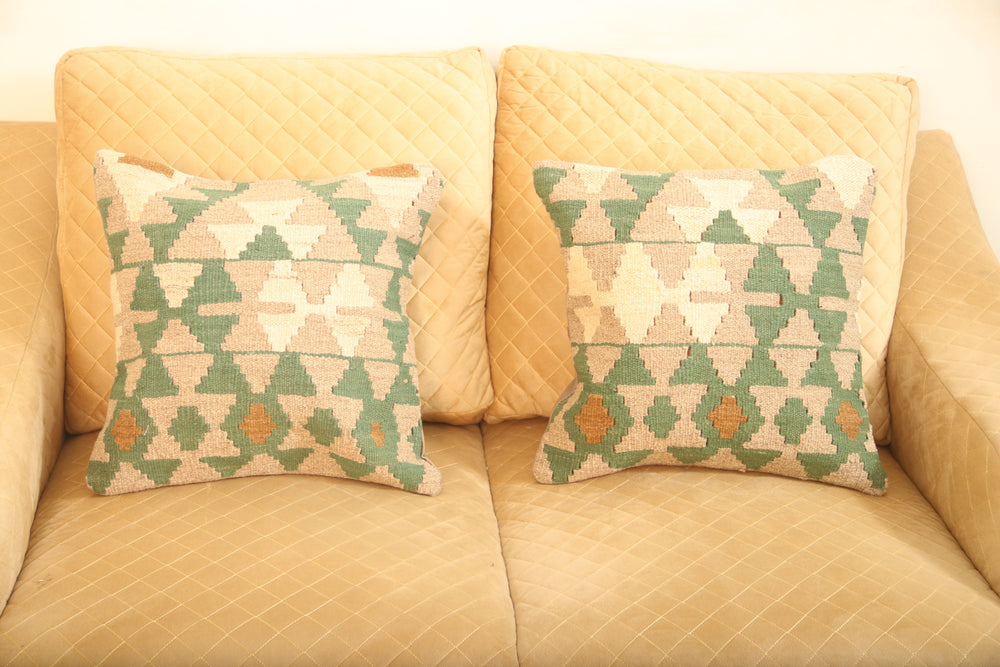 Green and beige geometric wool square cushion set of two with cream and rust accents displayed on a beige sofa.