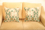Green and beige geometric wool square cushion set of two with cream and rust accents displayed on a beige sofa.